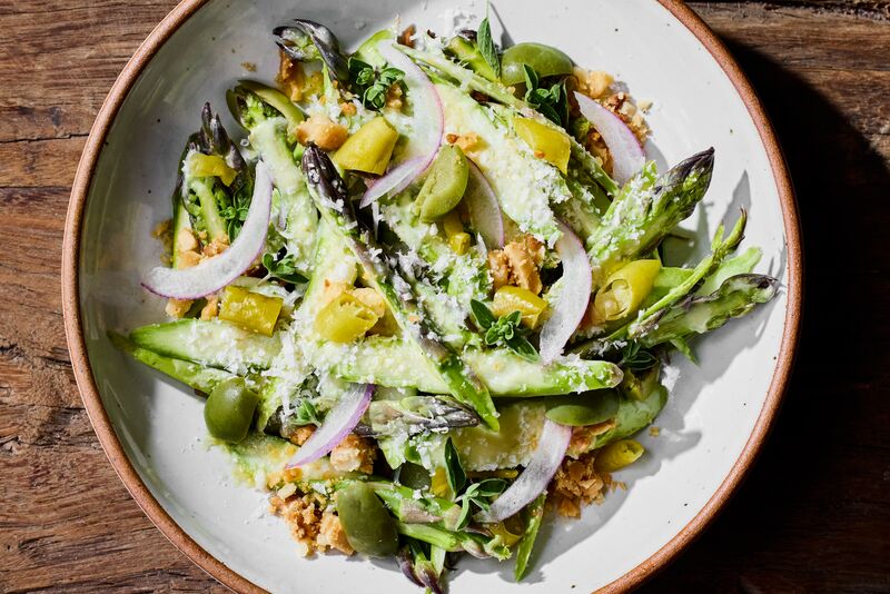 A plate of shaved asparagus salad with olives, red onion slices, herbs, and grated cheese.